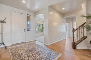 Foyer with light wood finished floors, baseboards, stairway, recessed lighting, and arched walkways