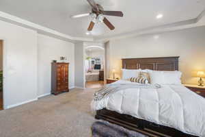 Bedroom with a tray ceiling, connected bathroom, arched walkways, baseboards, and light colored carpet