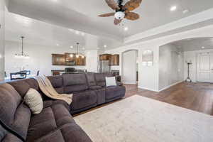 Living area featuring dark wood-type flooring, recessed lighting, ceiling fan with notable chandelier, and arched walkways