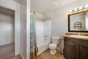 Full bath featuring visible vents, toilet, wood finished floors, shower / bath combination with curtain, and vanity