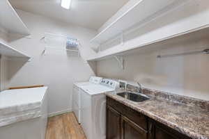 Laundry area with washing machine and clothes dryer, cabinet space, light wood-style floors, and a sink