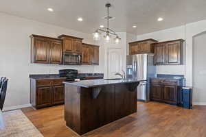 Kitchen with dark brown cabinetry, wood finished floors, appliances with stainless steel finishes, and a sink