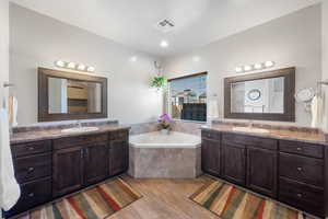 Full bathroom featuring a garden tub, two vanities, visible vents, and a sink