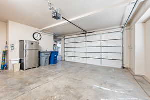 Garage featuring a garage door opener and freestanding refrigerator