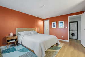 Bedroom with baseboards, light wood finished floors, and stacked washer / dryer