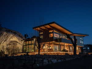 Back of house at night featuring stone siding and a balcony