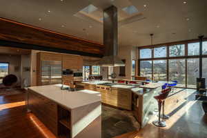 Kitchen with a large island, modern cabinets, appliances with stainless steel finishes, brown cabinetry, and a wood stove
