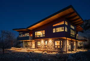 Back of house at twilight with stone siding and a balcony