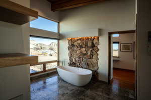 Bathroom featuring beam ceiling, a soaking tub, marble finish floor, and a towering ceiling