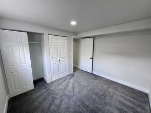 Unfurnished bedroom featuring baseboards, dark colored carpet, and a textured ceiling