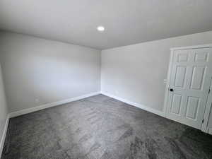 Spare room featuring baseboards, a textured ceiling, and dark carpet
