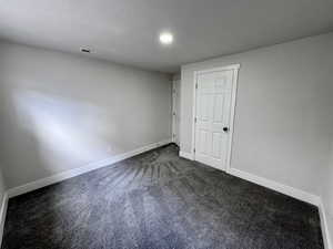 Unfurnished bedroom featuring dark colored carpet, visible vents, and baseboards