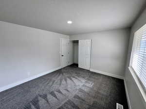 Unfurnished bedroom featuring baseboards, visible vents, dark carpet, and a textured ceiling