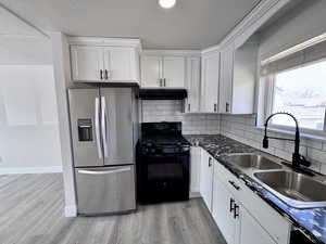 Kitchen featuring stainless steel fridge with ice dispenser, under cabinet range hood, white cabinets, gas stove, and a sink