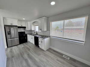 Kitchen with visible vents, black appliances, a sink, under cabinet range hood, and tasteful backsplash