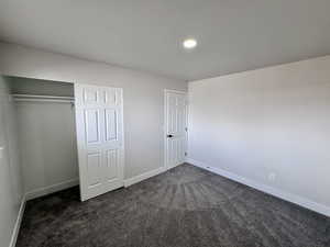 Unfurnished bedroom with a closet, dark carpet, a textured ceiling, and baseboards