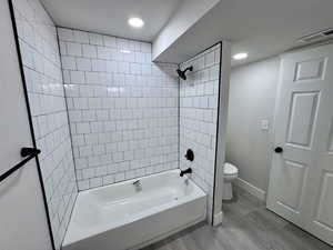 Full bath featuring visible vents, toilet, wood finished floors, washtub / shower combination, and baseboards