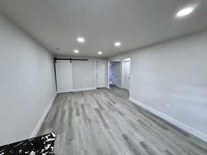 Unfurnished bedroom featuring recessed lighting, a barn door, baseboards, and light wood-style flooring