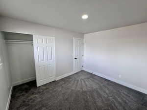 Unfurnished bedroom featuring a closet, dark carpet, a textured ceiling, and baseboards