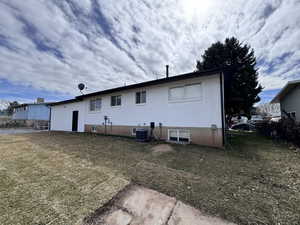 Rear view of property with brick siding, a lawn, and central AC