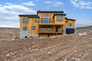 Back of house featuring stone siding and a balcony