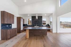 Kitchen featuring modern cabinets, a high ceiling, a kitchen island with sink, dark stone counters, and decorative backsplash