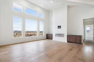 Unfurnished living room featuring a high ceiling, light wood-style flooring, healthy amount of natural light, and recessed lighting