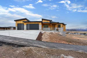 Contemporary house with stone siding, concrete driveway, an attached garage, a porch, and a mountain view