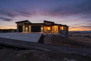 Contemporary house with stone siding, concrete driveway, a garage, and covered porch