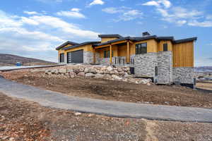 Modern home with stone siding, a garage, a chimney, a mountain view, and driveway