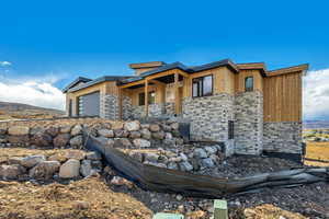 Contemporary house featuring stone siding, covered porch, and a garage