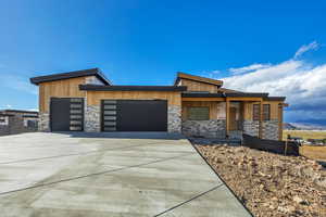View of front of property with stone siding, an attached garage, concrete driveway, and a porch