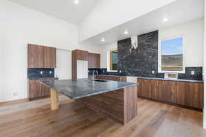 Kitchen featuring modern cabinets, wood finish cabinets, dark stone counters, a center island with sink, and recessed lighting