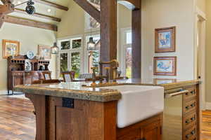 Kitchen featuring light stone countertops, brown cabinets, wood finished floors, high vaulted ceiling, and a sink