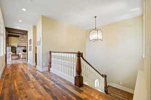 Hallway with baseboards, an upstairs landing, an inviting chandelier, and dark wood-style flooring