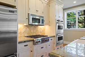 Kitchen with baseboards, backsplash, appliances with stainless steel finishes, and light stone countertops