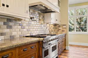 Kitchen with tasteful backsplash, a healthy amount of sunlight, premium range hood, double oven range, and brown cabinetry