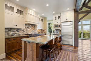 Kitchen with a kitchen island, glass insert cabinets, light stone countertops, built in appliances, and dark wood-style flooring