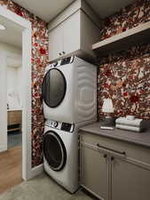 Laundry room featuring stacked washer / dryer, wallpapered walls, cabinet space, and light tile patterned floors
