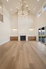 Unfurnished living room with light wood-type flooring, a fireplace, high vaulted ceiling, a chandelier, and recessed lighting