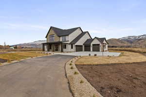 Modern farmhouse style home featuring a porch, asphalt driveway, a mountain view, stone siding, and a front yard