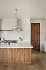 Kitchen with brown cabinetry, a textured ceiling, light wood-type flooring, white cabinets, and decorative light fixtures