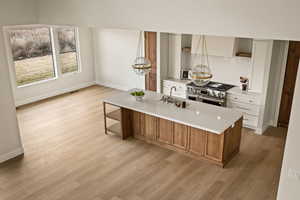 Kitchen featuring a center island with sink, double oven range, a breakfast bar, light wood-type flooring, and light stone countertops