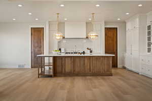 Kitchen featuring an island with sink, brown cabinetry, decorative light fixtures, white cabinets, and recessed lighting