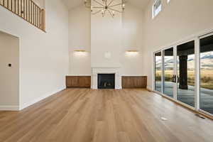 Unfurnished living room with light wood-style floors, a chandelier, a fireplace, and high vaulted ceiling