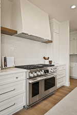 Kitchen featuring custom exhaust hood, white cabinets, double oven range, light wood finished floors, and recessed lighting