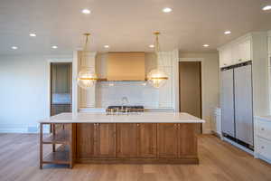 Kitchen with a kitchen island with sink, brown cabinetry, high end refrigerator, recessed lighting, and decorative light fixtures