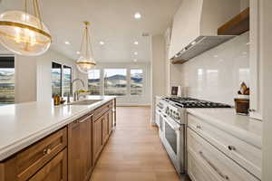 Kitchen with stainless steel range with gas cooktop, recessed lighting, wall chimney exhaust hood, hanging light fixtures, and white cabinets