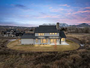 Back of house at dusk with a mountain view, a patio, and a yard
