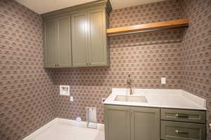 Washroom with wallpapered walls, washer hookup, and cabinet space